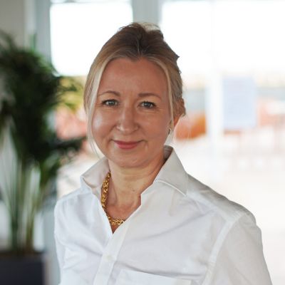 A photograph of Lindsay Hooper, CISL's CEO, she stands side-on to the camera in a white collared shirt smiling, her blonde hair is tied back and behind her you can see some shrubbery.  She appears calm, friendly and professional. 