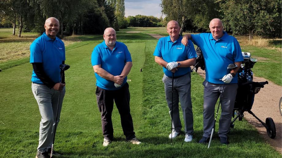 Four people in blue shirts standing next to each other on a golf course looking at the camera.