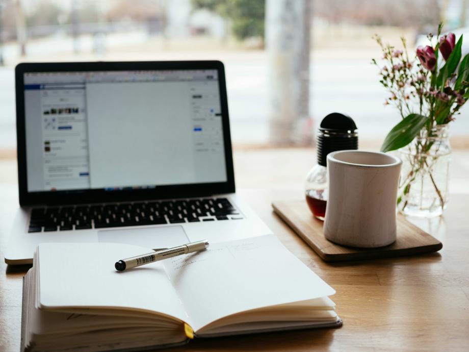 Desk with laptop, notebook & pen, and mug of coffee