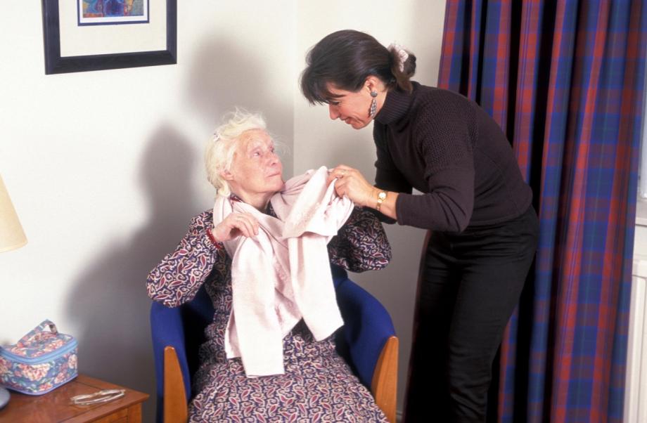 Woman helping her elderly mother put a jumper on