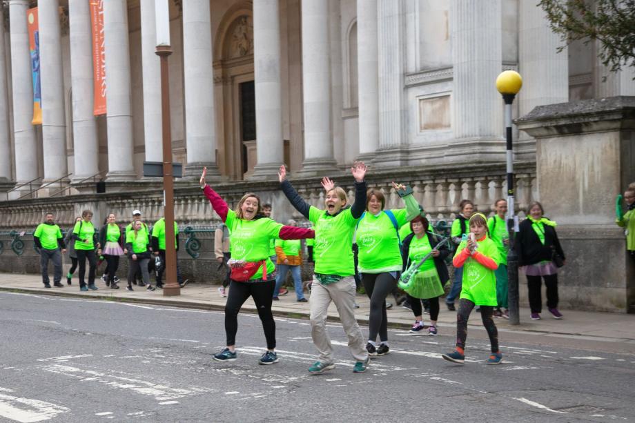 People wearing bright green on a zebra crossing near a large building 