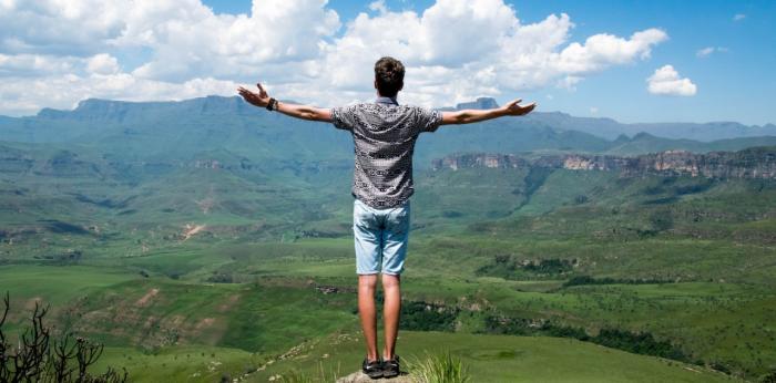 Young man standing on mountaintop with arms open wide across countryside view