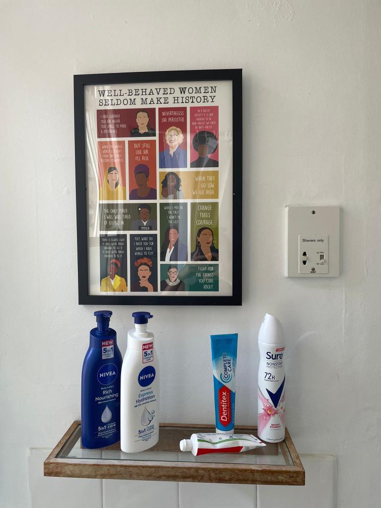 Women's toiletries on a shelf in front of poster containing images of powerful women.