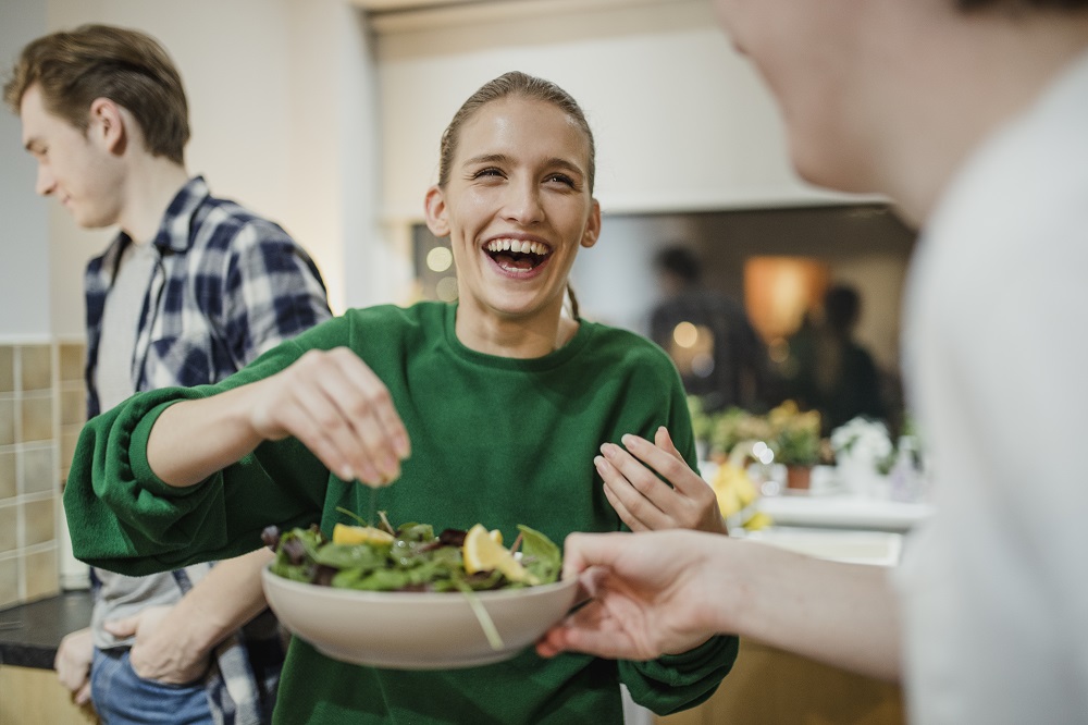 Happy woman preparing vegan salad with friends