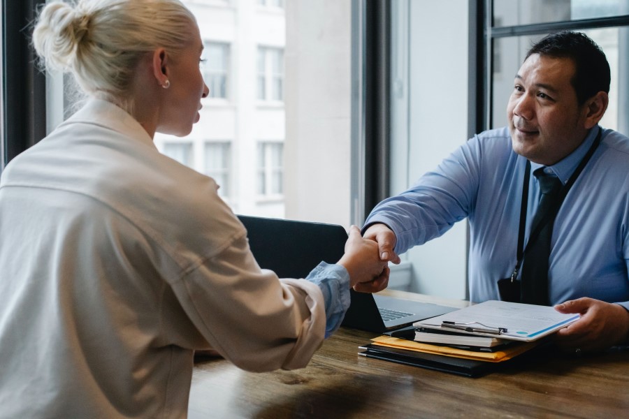 A man and woman shake hands over a desk.