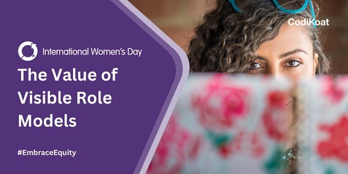 A title image showing the headline "The Value of Visible Role Models" on the left with the International Women's Day logo above the headline and #EmbraceEquity below it. On the right, there is an image of a woman wearing glasses on her head peering over the top of a floral notebook