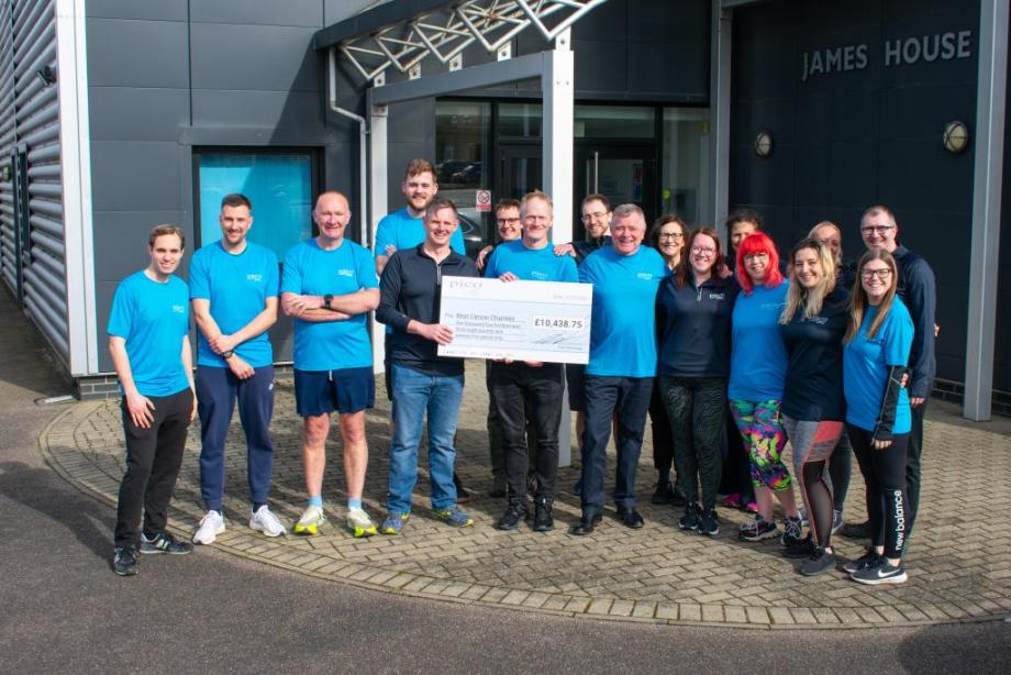 an image of several Pico Technology employees wearing running tops outside the headoffice and holding a large foamboard cheque