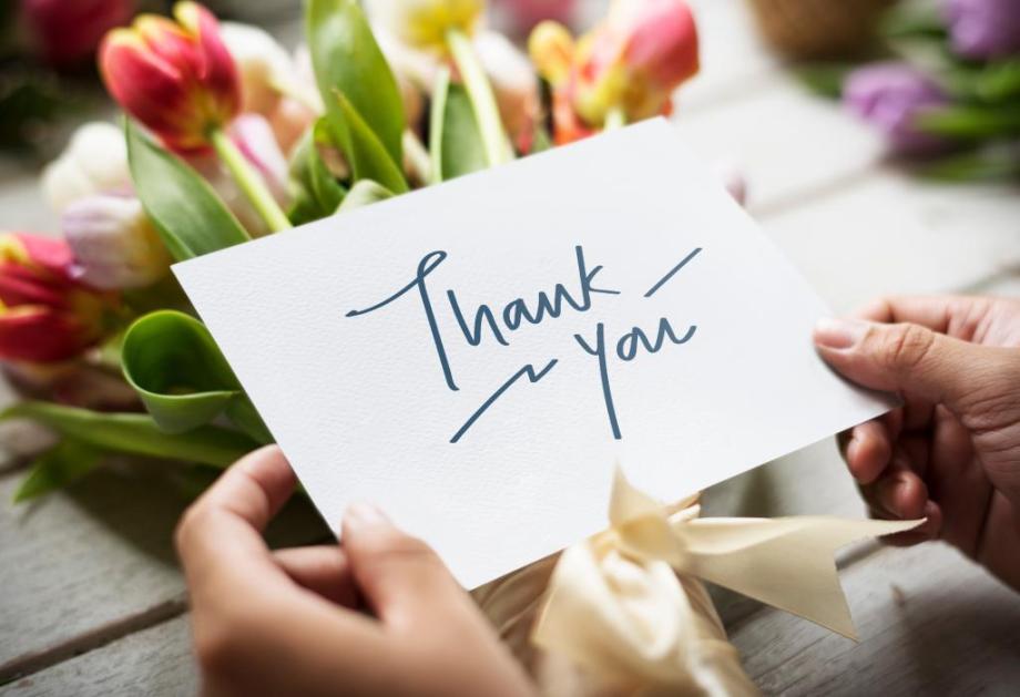 tulips on a table with a feminine hand holding a white card that says Thank You written on it