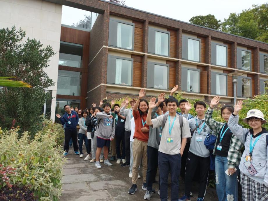 Students of Cambridge international academy's 2023 summer school stand in front of buildings and wave at the camera