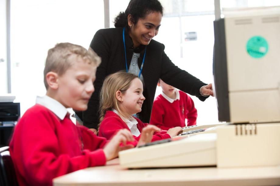 Children smile as a teacher points something out on a computer screen