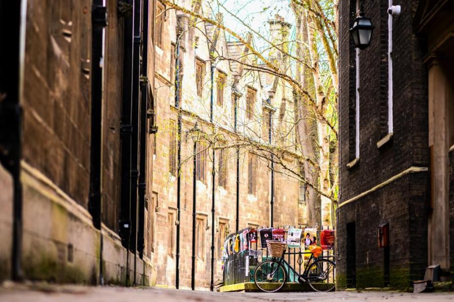 Meet Cambridge - looking through an old brick arch at ground level where there is a black framed bicycle with a wicker basket leaning against black iron railings