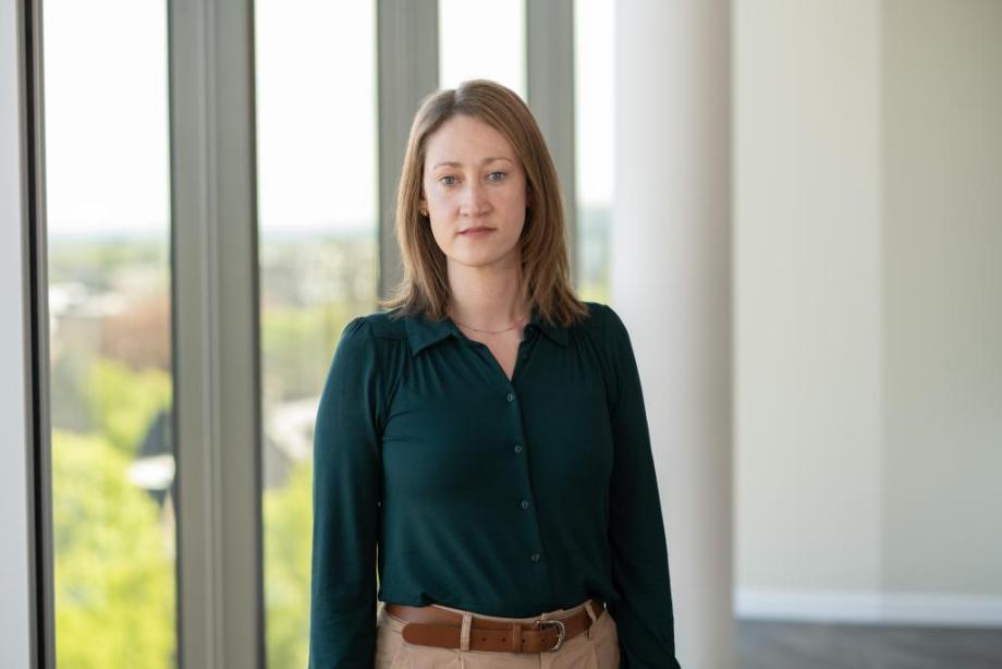 Lady with straight hair stood in front of a window in a dark green shirt 