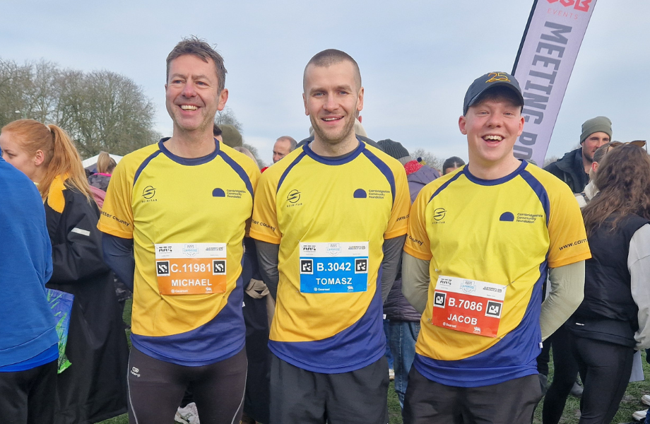 Three runners in Cambridgeshire Community Foundation branded yellow and navy running tops standing in a crowd of runners.