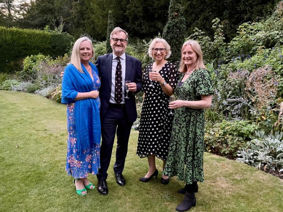 3 white woman and 1 white mean standing in a College garden smiling at the camera with drinks in their hands