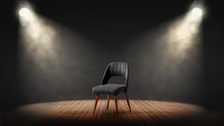 A single chair is spotlit on a stage