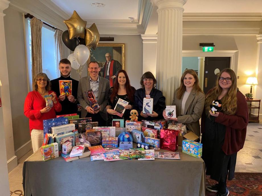 A mix of men & women smiling into the camera holding toys behind a table laden with toys