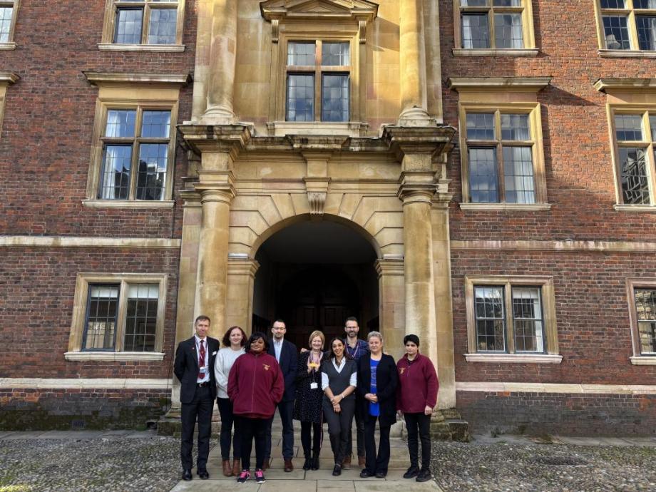 St Catharine's College team in Cambridge standing outside an old part of the college with red brick & yellow arch way