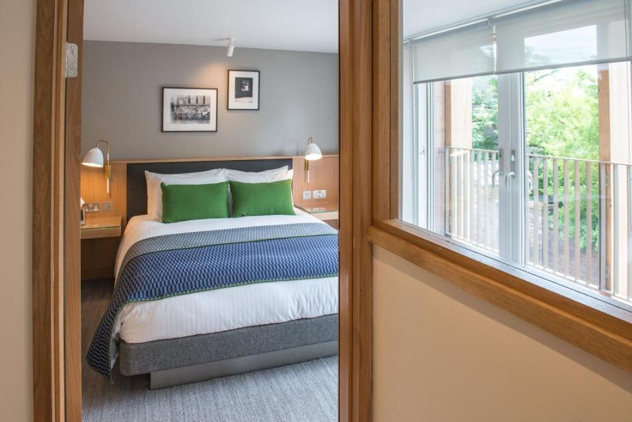 An award winning en suite bedroom at Jesus College Cambridge, West Court. The room has large windows and the room is light, bright & airy. There is a double bed in the middle with white linen & emerald scatter cushions