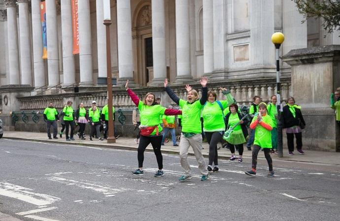 Group of adults and children wearing green t-shirts crossing a road near Fitzwilliam Museum
