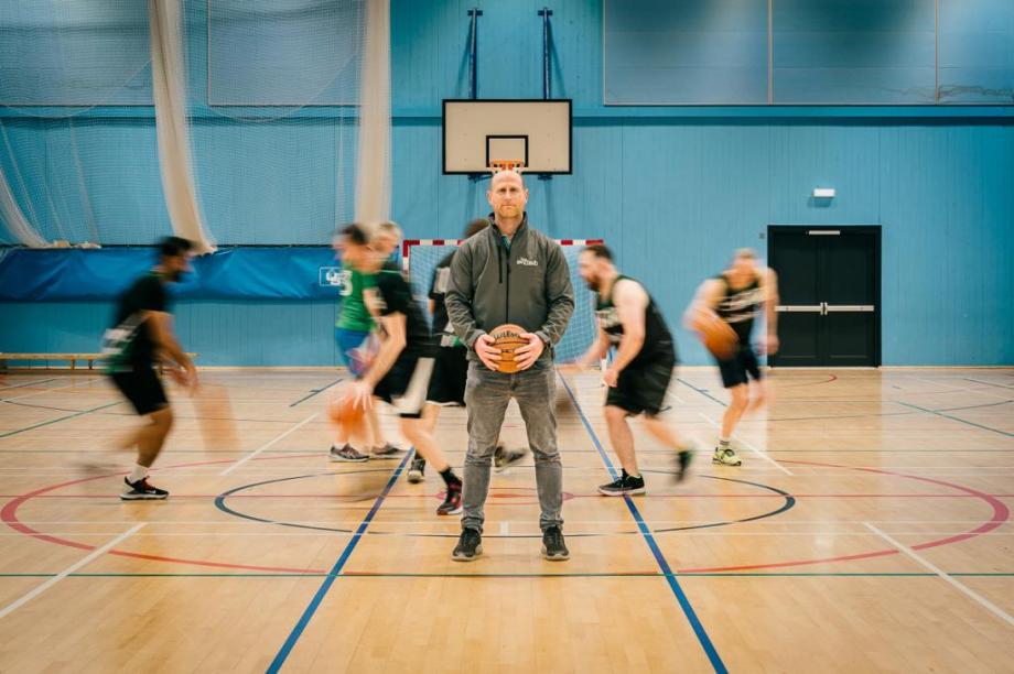 Northstowe Jets doing drills, blurred in background, with Marc Mann, Founder of SkyTech Cambridge standing in front holding a basketball