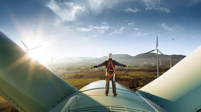 Man stands on top of aeroplane and spreads his arms, looking out on a wind farm