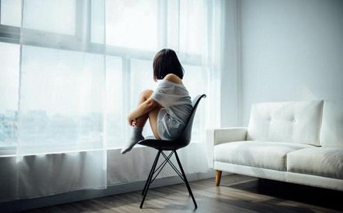 woman sitting in an empty room and looking out of a window