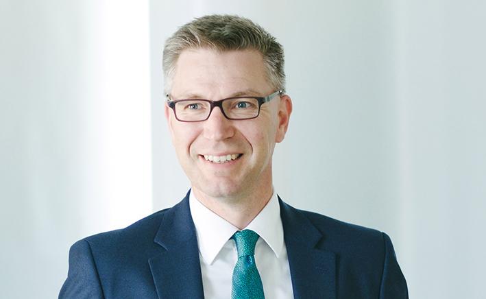 Man in a blue suit and square glasses smiling 