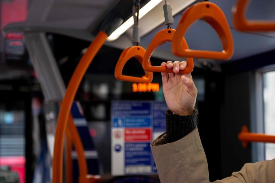 Person holding an overhead grab handle on a bus